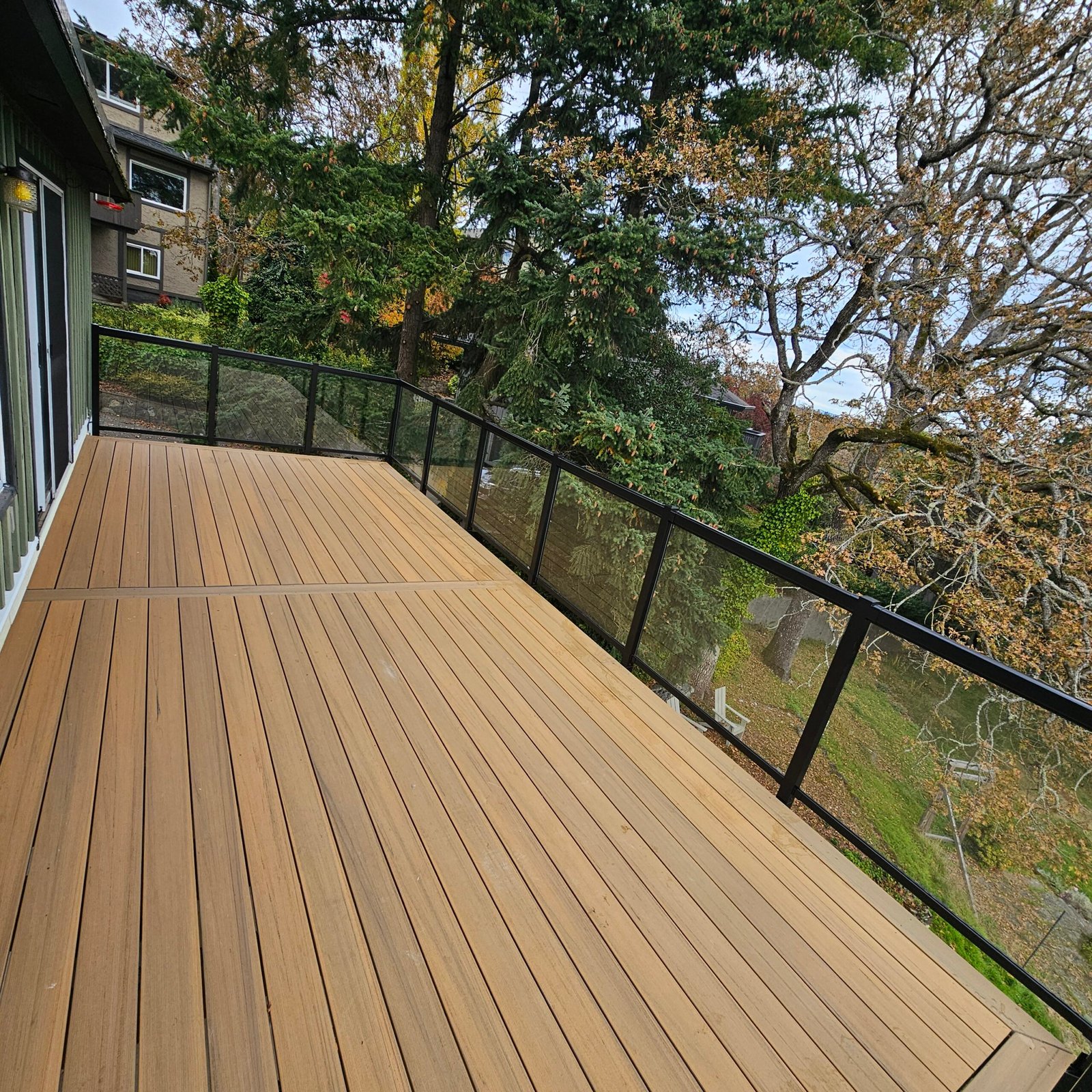 Warm-toned deck with black-framed glass railings overlooking a wooded garden